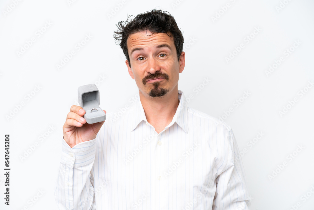 Young man holding a engagement ring isolated on white background with sad expression Young man holding a engagement ring isolated on white background with sad expression