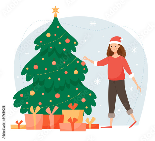 A cute girl in a red santa claus hat decorates the Christmas tree. Winter scene with a decorated Christmas tree and many gifts. Merry Christmas and a happy new year. 