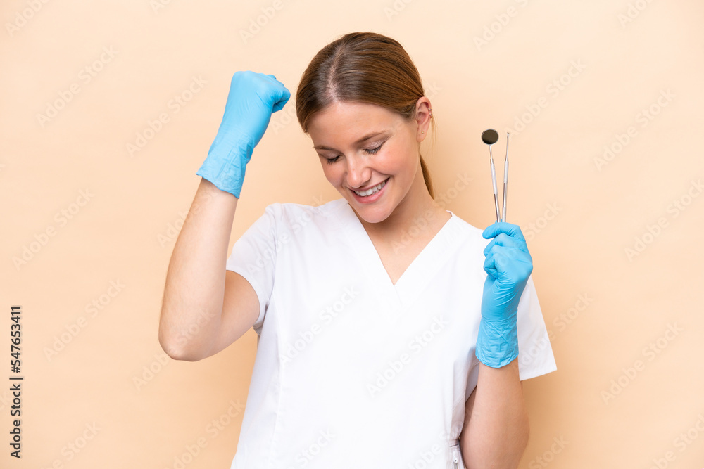 Dentist caucasian woman holding tools isolated on beige background celebrating a victory Dentist caucasian woman holding tools isolated on beige background celebrating a victory