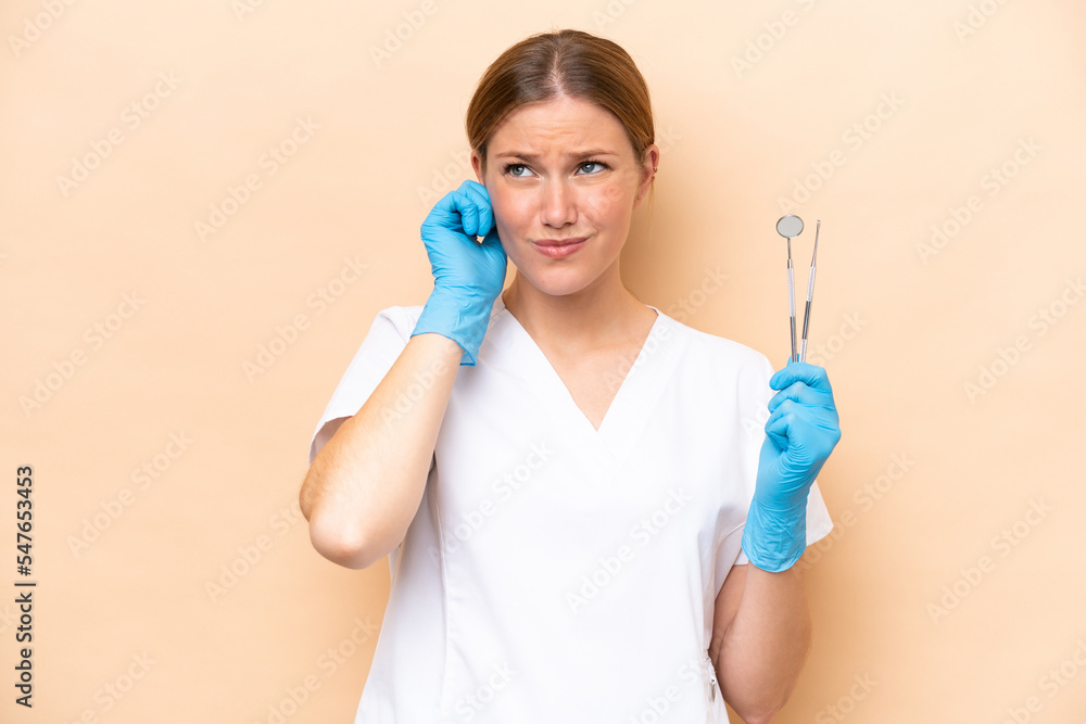 Dentist caucasian woman holding tools isolated on beige background frustrated and covering ears Dentist caucasian woman holding tools isolated on beige background frustrated and covering ears