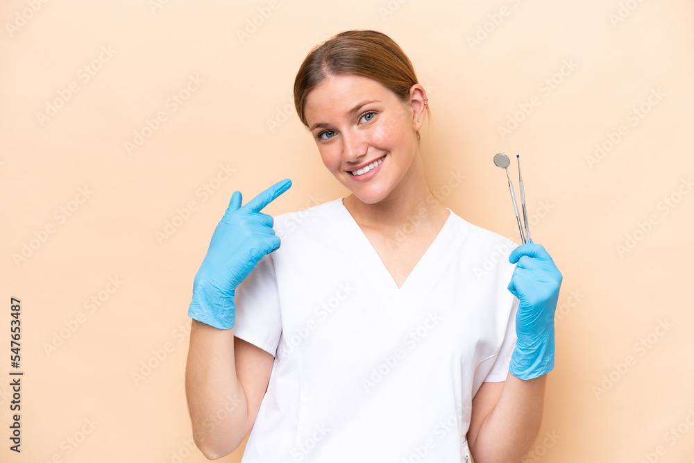 Dentist caucasian woman holding tools isolated on beige background giving a thumbs up gesture Dentist caucasian woman holding tools isolated on beige background giving a thumbs up gesture