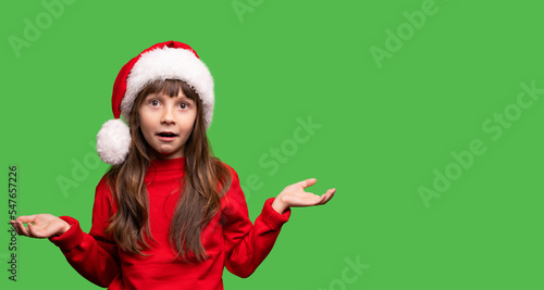 Disappointment gesture. The girl in the Santa hat opened her mouth and opened her arms in different directions. Emotional portrait of a child. Expectation and reality did not match. No gifts