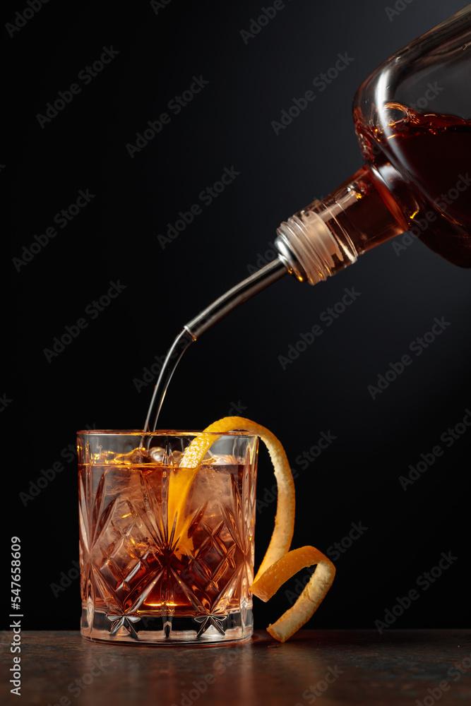  Whiskey is poured into a glass with ice and orange peel. - obrazy, fototapety, plakaty 
