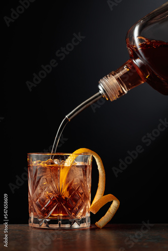  Whiskey is poured into a glass with ice and orange peel.