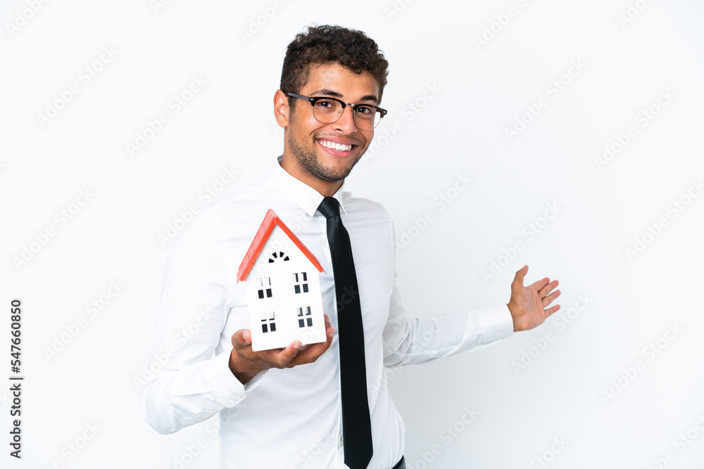 Young business Brazilian man holding a house toy isolated on white background extending hands to the side for inviting to come Young business Brazilian man holding a house toy isolated on white background extending hands to the side for inviting to come