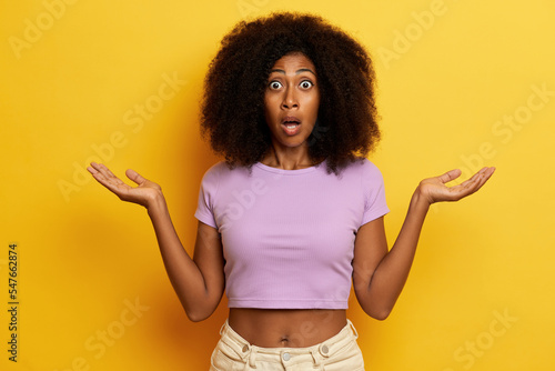Billede på lærred Shocked curly haired woman keeps mouth opened with hands aside in hesitant gestu