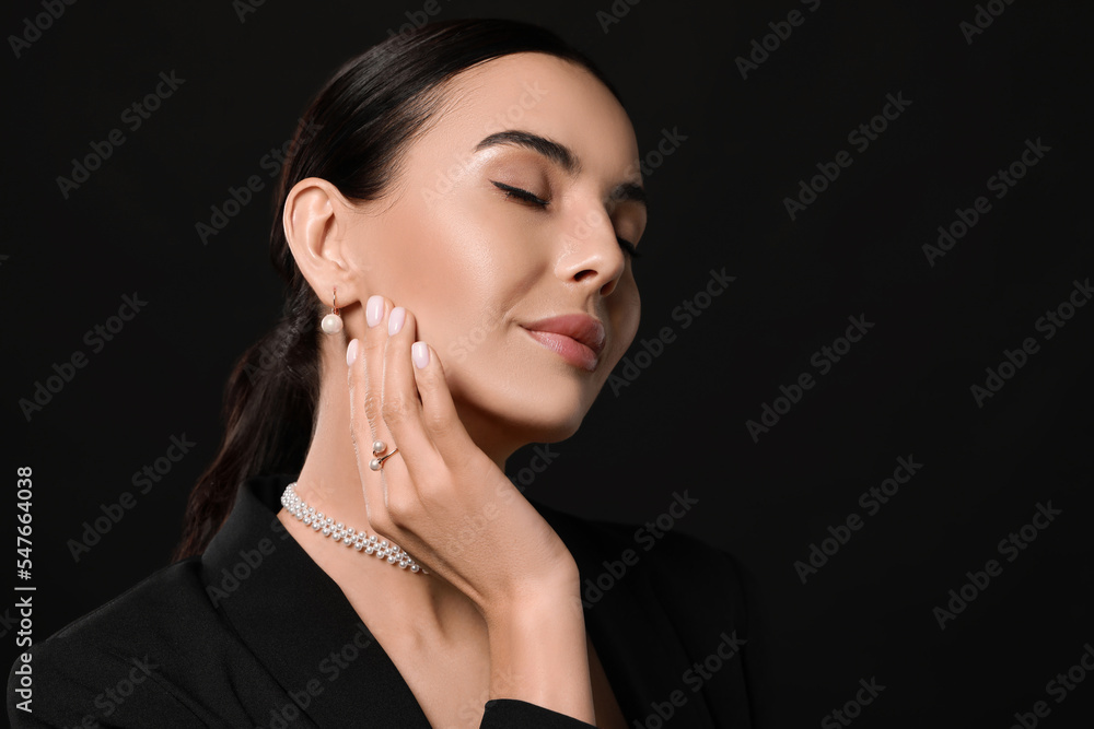 Young woman with elegant pearl jewelry on black background, space for text