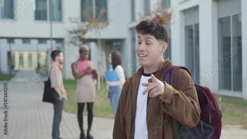 student boy looking at camera while his friends are behind talking, in university campus