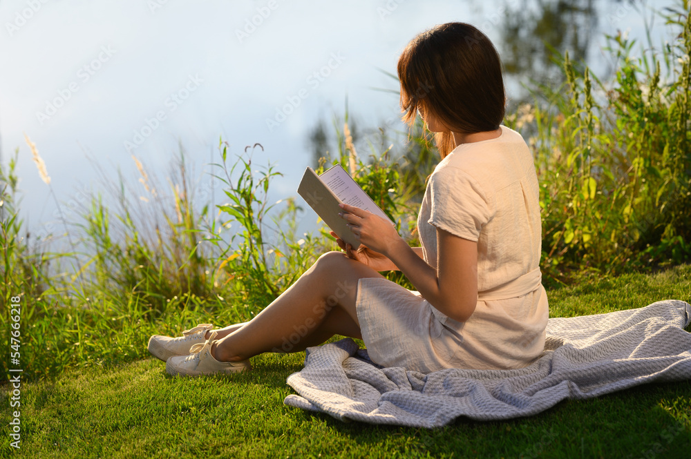 Young woman reading book near lake on sunny day Young woman reading book near lake on sunny day