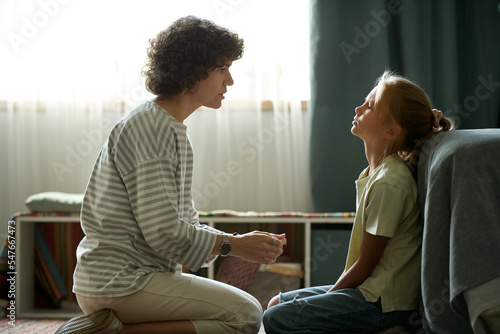 Young mother having conversation with her difficult daughter while they sitting in the room photo