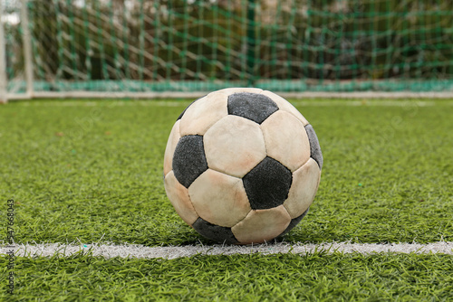 Dirty soccer ball on green football field against net