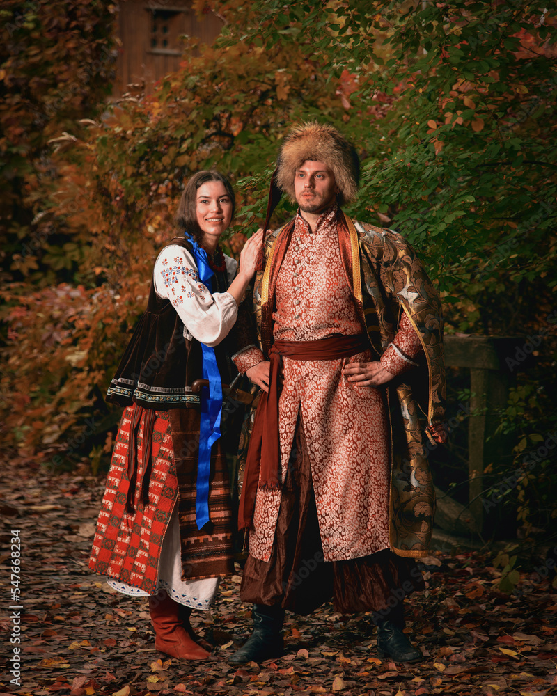 Young smiling couple dressed traditional ukrainian clothing. Cossack man and woman in embroidered costumes outdoors. Vintage outfit.