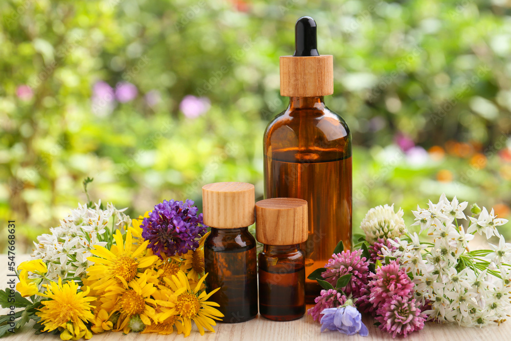 Bottles of essential oil and different flowers on white wooden table outdoors, closeup Bottles of essential oil and different flowers on white wooden table outdoors, closeup