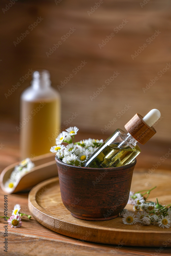 Bottle of chamomile essential oil and flowers on wooden table Bottle of chamomile essential oil and flowers on wooden table