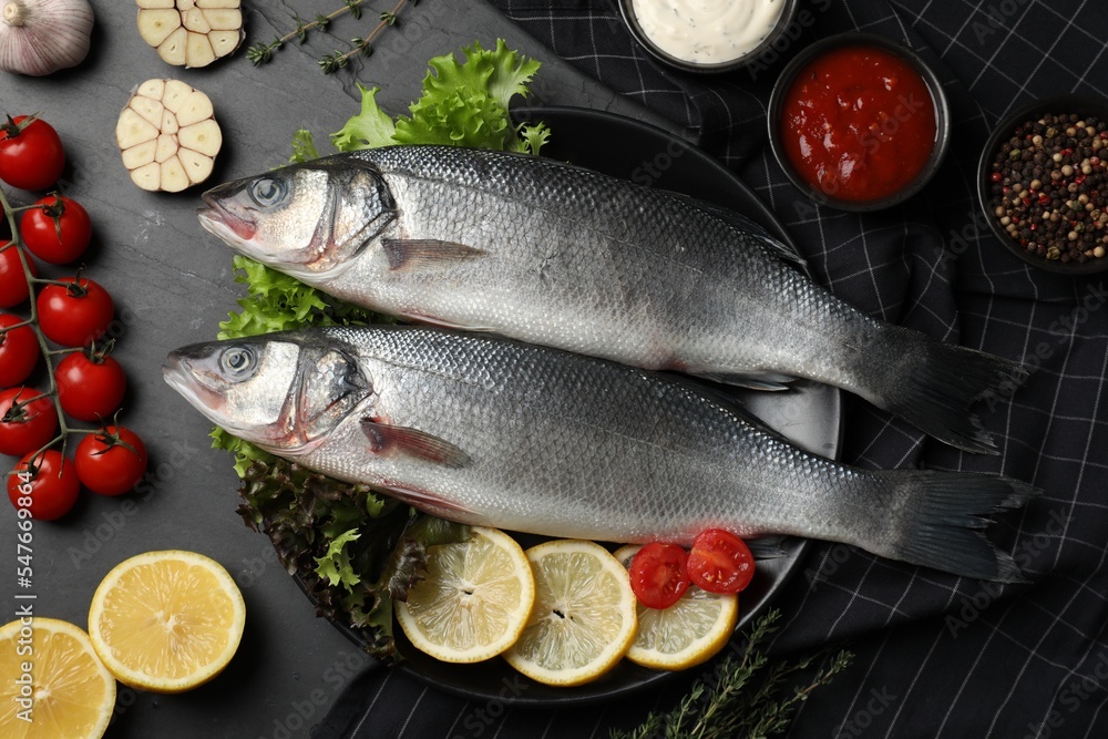 Fresh raw sea bass fish and ingredients on black table, flat lay Fresh raw sea bass fish and ingredients on black table, flat lay