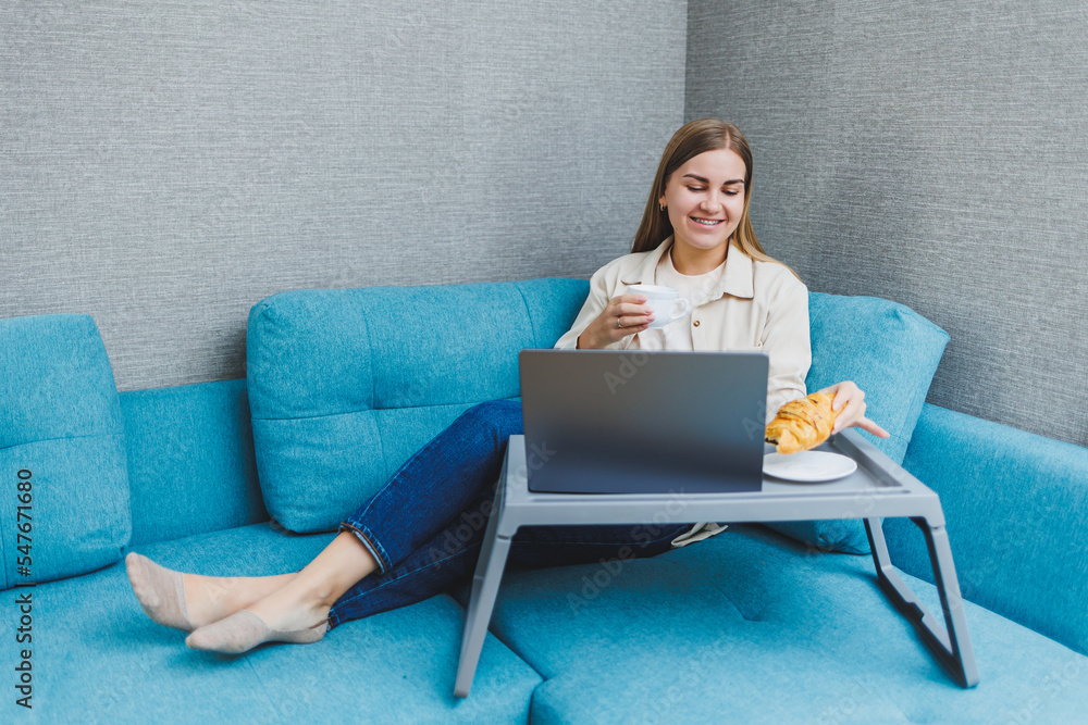 Smiling woman using laptop to check e-mail news online while sitting on sofa, working on computer, writing blog or watching webinar, studying at home Smiling woman using laptop to check e-mail news online while sitting on sofa, working on computer, writing blog or watching webinar, studying at home