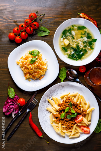 three-course set on a table. Tasty lunch set made of three meals, such as Green Sorrel soup, salad and pasta penne bolognese