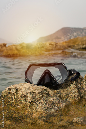 Diving mask on a coral rock in the ocean with sunset light
