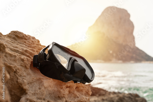 Diving mask on a coral rock with the Mediterranean sea and the great stone of Ifach in Calpe in the background © Julian