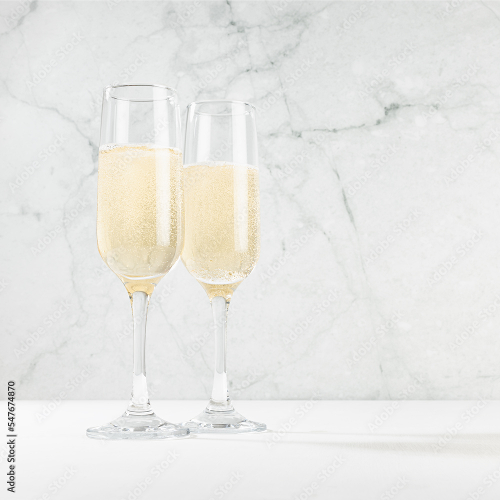 Christmas festive background with two sparkling champagne wine glass in modern white bar interior with marble, copy space, square. Holiday beverage for congratulations and party. - obrazy, fototapety, plakaty 