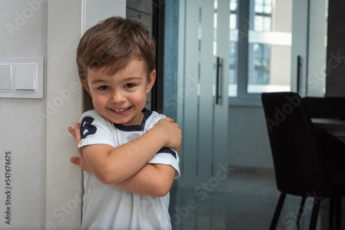 a small, cute, emotional boy is standing in the corridor, leaning against the wall, surprised, moving his hands, smiling. Close-up portrait view