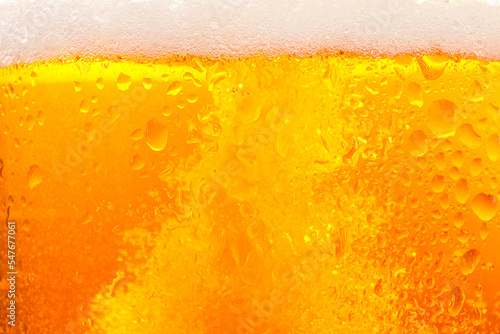 Glass of tasty cold beer with foam and condensation drops as background, closeup