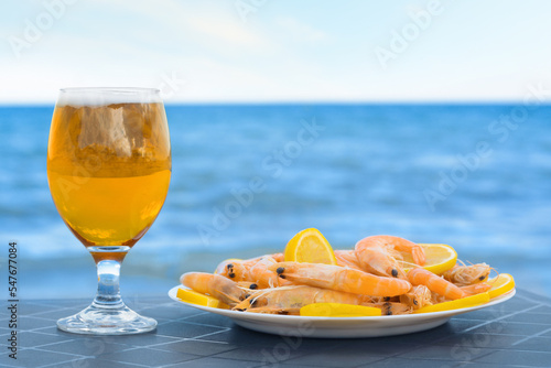 Cold beer in glass and shrimps served with lemon on beach