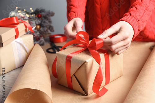 Christmas present. Woman tying ribbon bow on gift box at table, closeup