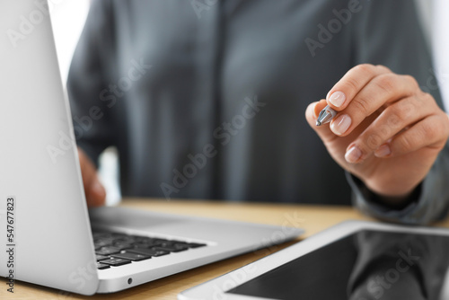 Woman with tablet and pen working on laptop at wooden table, closeup. Electronic document management