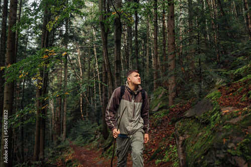 A handsome young man in casual clothes walks through the forest in the mountains with a serious face and looks away. Hiking trips alone.