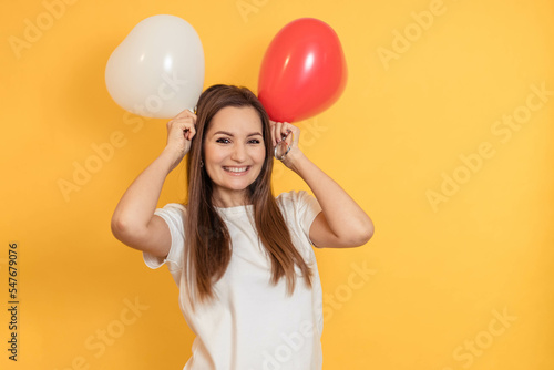 Funny portrait of a young girl with two heart-shaped balloons on a yellow background, copy space © Natalia