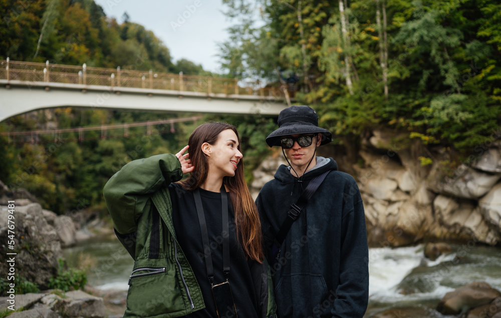 Portrait of a beautiful couple of happy tourists in casual clothes standing in the mountains on a rock against the background of a fast mountain river.