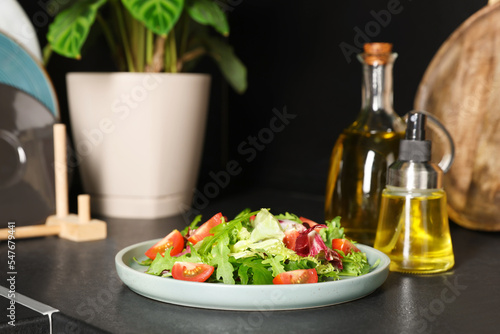 Plate of salad and bottles with cooking oil on black table in kitchen