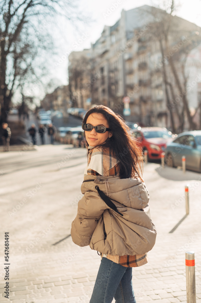 Cheerful woman in warm spring clothes walks down the sunny street and looks at the camera with a smile on her face.Vertical