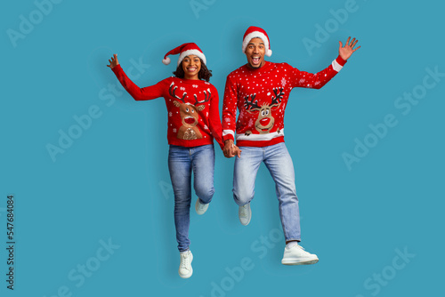 Emotional black couple holding hands and jumping up, celebrating Christmas