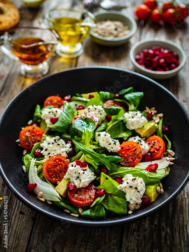 Fresh vegetable salad with feta cheese and pomegranate on wooden table 