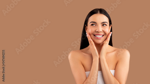 Smiling half-naked pretty brunette lady touching her cheeks, empty space