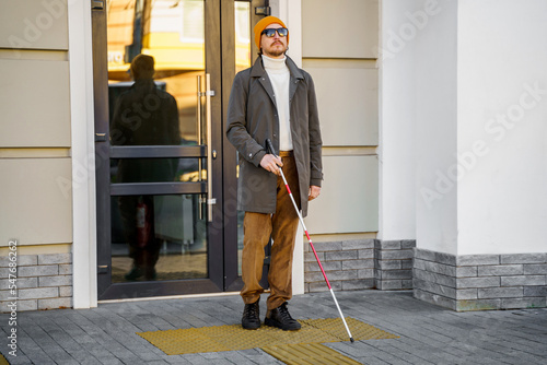 Blind man with a walking stick. Stands on a tactile tile for self-orientation while moving through the streets of the city