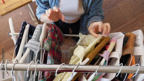 Woman sorting and picking pre owned clothes for resale or donation, top down view of clothes hanging on rail.
