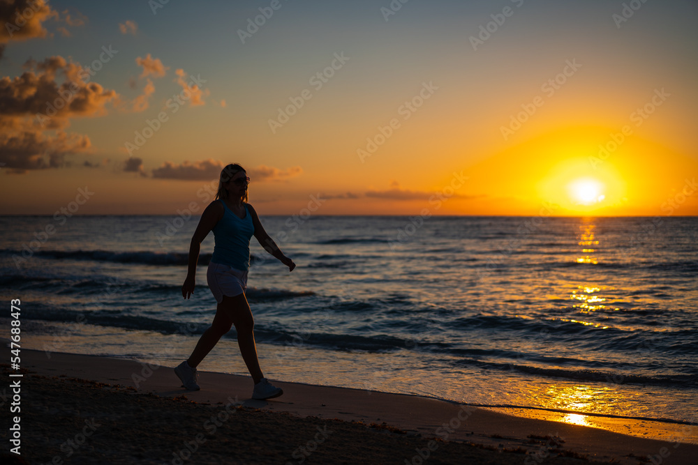 Fototapeta premium Woman walking on sunny, tropical beach at daybreak 