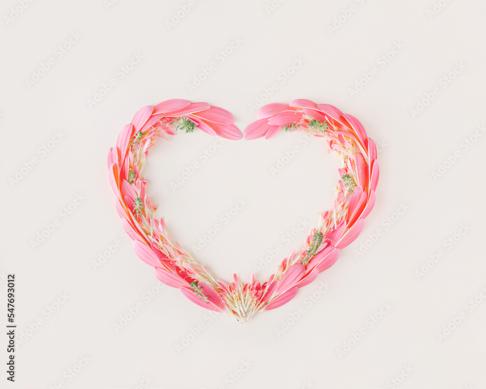 Heart-shaped frame made with pink petals and twigs with green leaves on an isolated pastel beige background. Minimal flat lay. Floral love symbol. Wedding or valentines day card. Blooming concept.