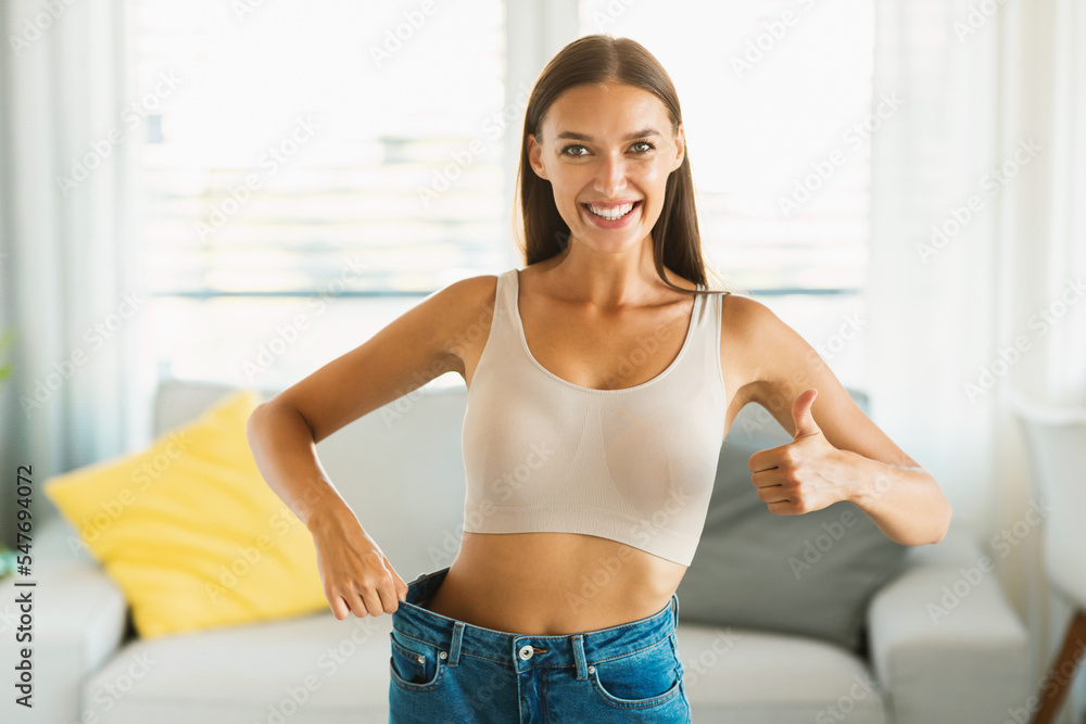 Great diet concept. Happy caucasian woman after weight loss gesturing thumbs up and comparing jeans size after slimming