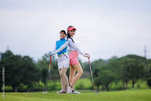 Two young asian women professional golfers stand and pose looking at camera and smiling taking photo at the golf course