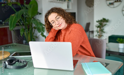 Young smiling pretty woman student using laptop elearning or remote working at home office looking at laptop computer watching webinar, learning web course, studying online sitting at table. photo