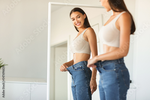 Excited young fit woman losing weight and wearing old big jeans, woman feeling satisfied with results of her slimming