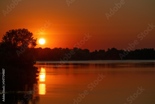Orange-red sunset over the Dnieper river and forest in Ukraine. The light of the sun is reflected in the water