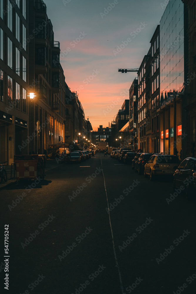 Blick einer Straße mit Autos am Abend in der Dämmerung und der Spiegelung der Sonne in den Gebäuden Blick einer Straße mit Autos am Abend in der Dämmerung und der Spiegelung der Sonne in den Gebäuden