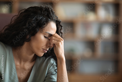Upset brunette curly woman suffering from headache while working