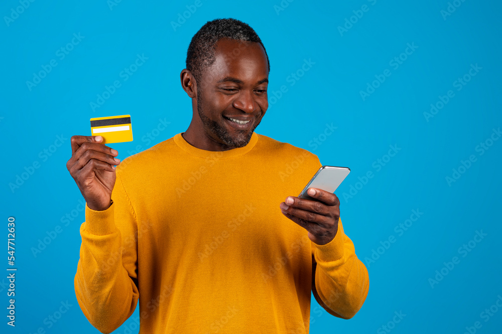 Smiling black man holding smartphone and credit card Smiling black man holding smartphone and credit card