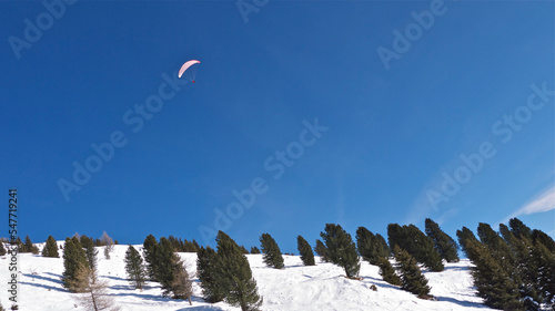 A paraglider under a parachute dome slowly flies over the mountains. A parachutist flies over the ski slopes of the Austrian mountains. Ski slopes of the Austrian Alps. December 31, 2010: Austria, Alp